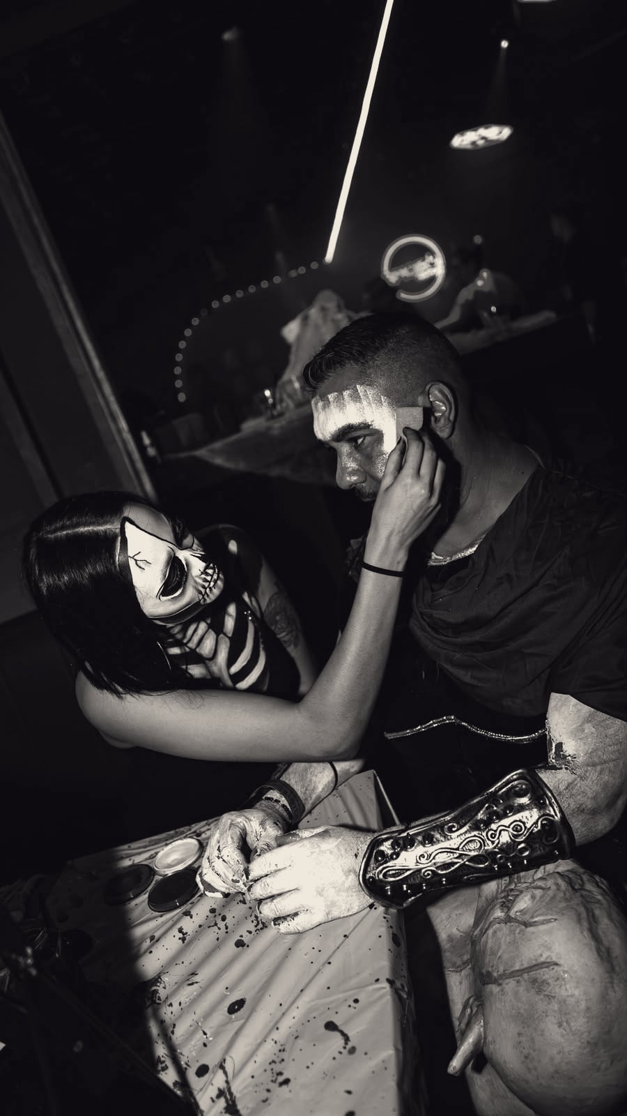 Gaia painting a skull design onto a man in costume at an event