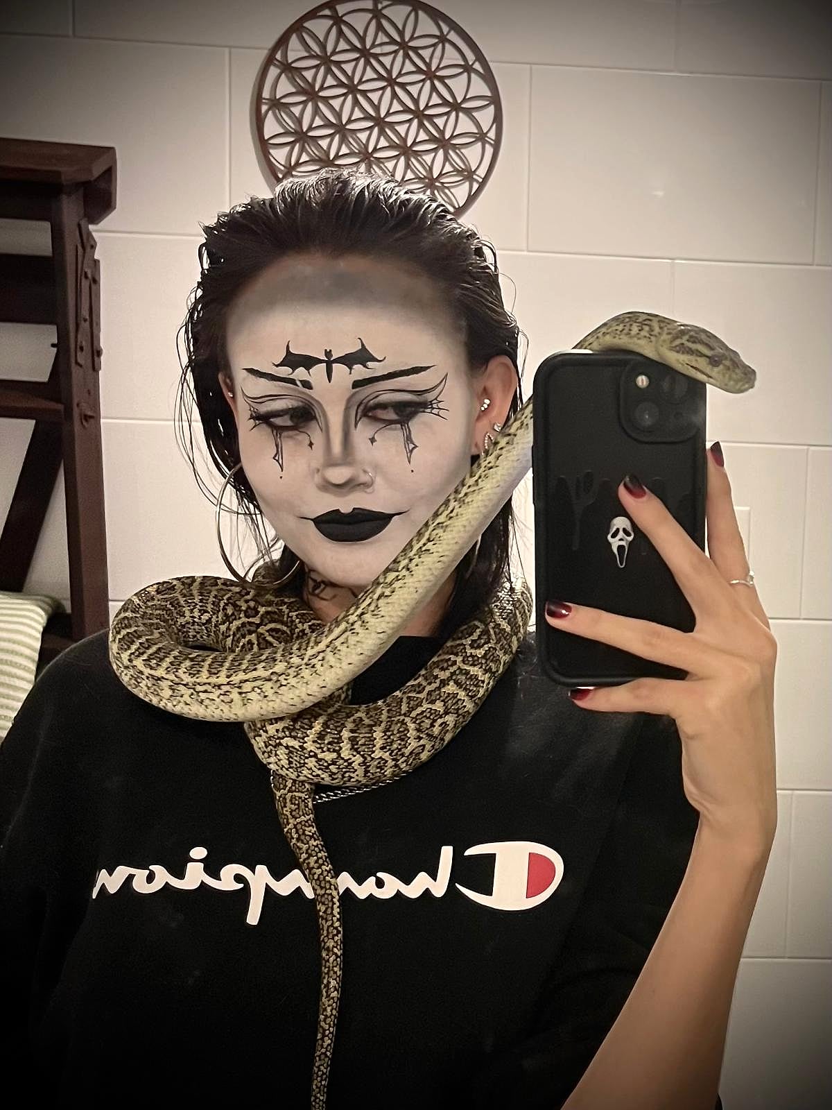 Gothic face paint on a white base, with a bat motif on the forehead and winged liner, worn with a live carpet python
