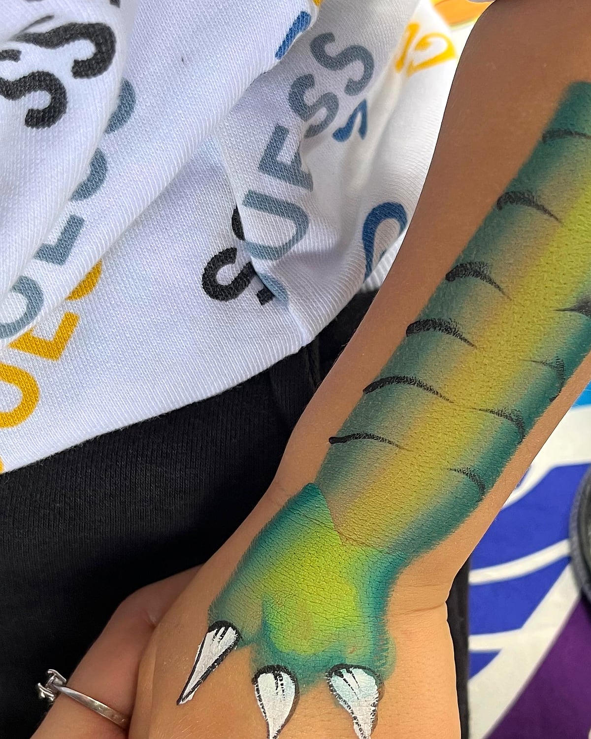 A green dragon painted down a child's forearm, with white claws over the knuckles