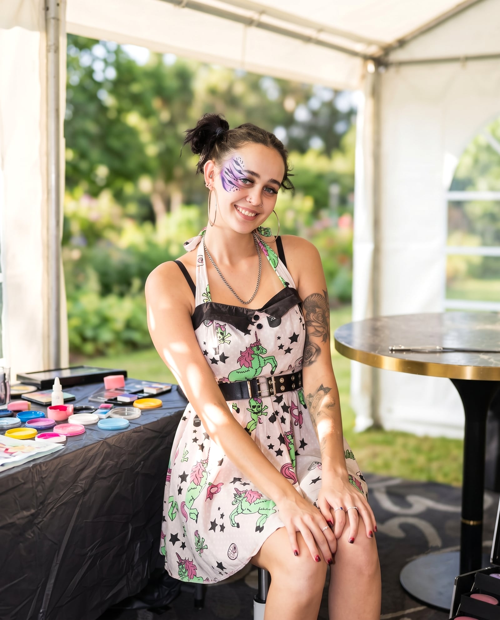 Gaia sitting at her face-painting table under a marquee, paints laid out in front of her