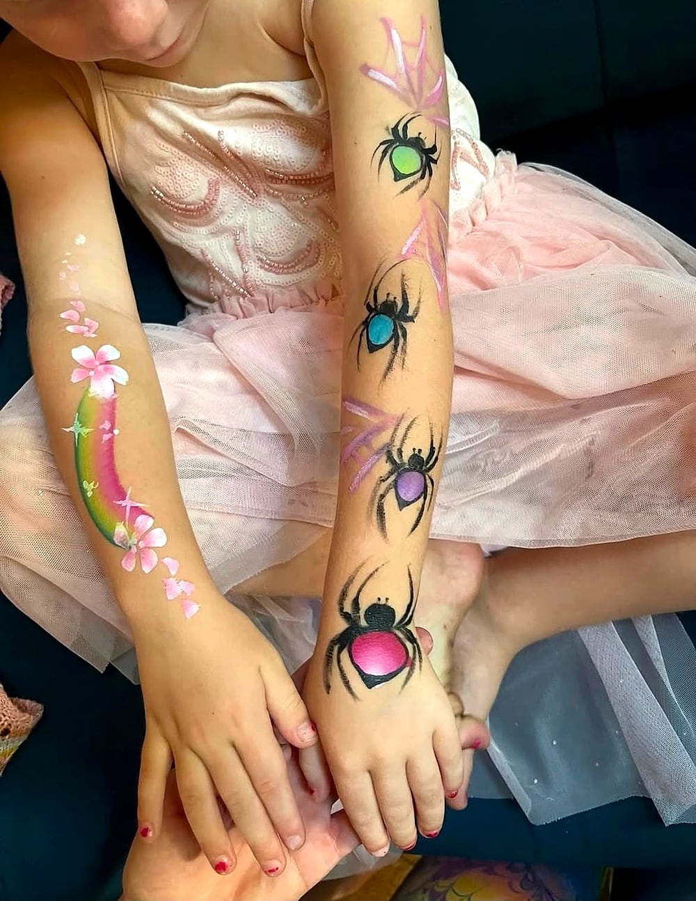 Coloured spiders painted along one arm and a rainbow and blossom along the other