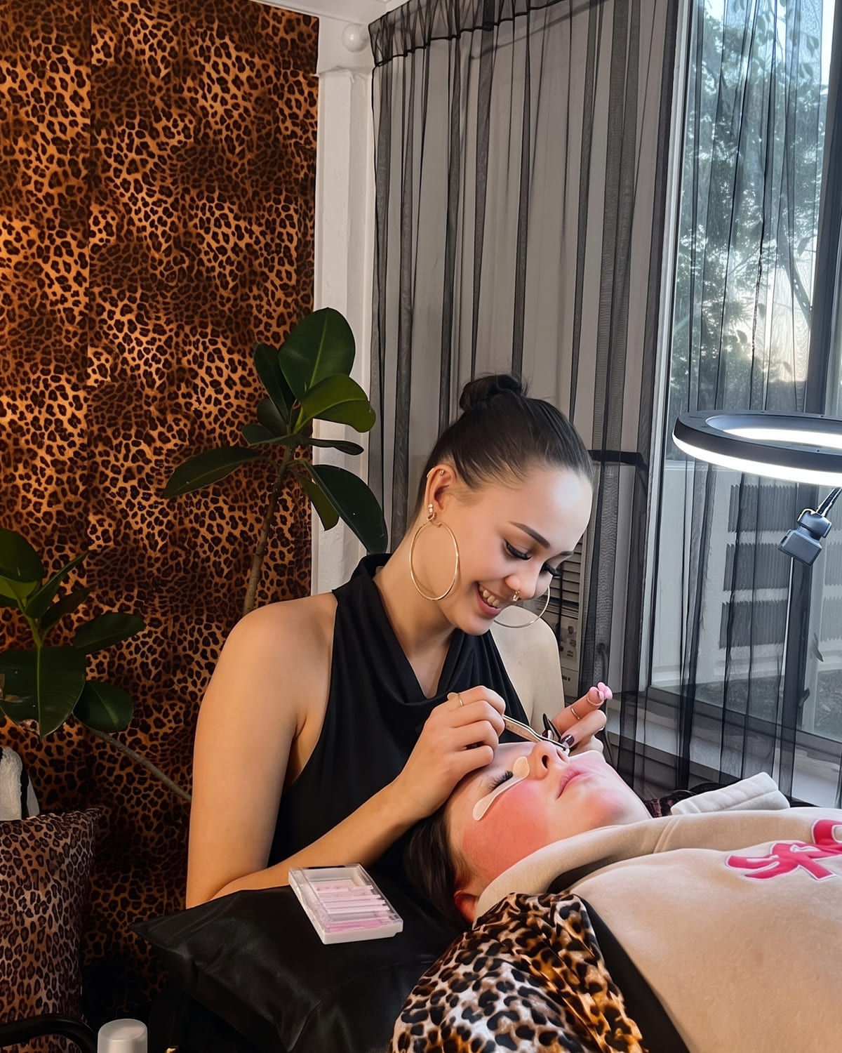 Gaia applying lash extensions to a client in her Redcliffe studio, with the leopard-print wall behind her